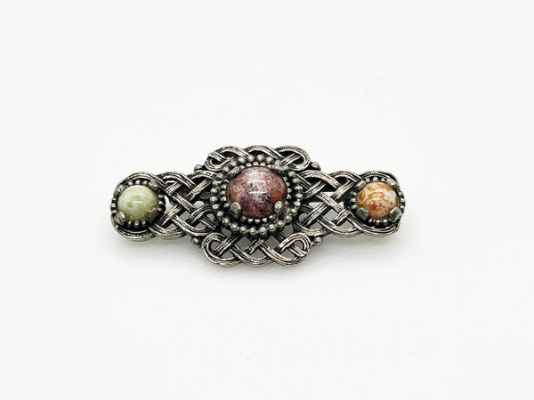 Embellish your style with the elegant and enduring Vintage Celtic Knot Style Brooch Art Glass. This beautifully crafted brooch features textured metal encasing stunning round stones in shades of pale green, red, and gold-amber. Measuring at 1.75", this accessory will add a touch of sophistication to any ensemble. Perfect for those seeking a refined and timeless addition to their collection.