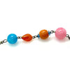 A close-up of a beaded chain featuring translucent glass beads in bright blue, orange, and pink, separated by small dark metal spacers on a white background.