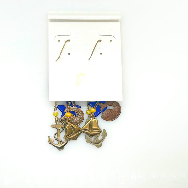 Vintage Cookie Lee nautical charm dangle earrings in antiqued brass with anchor, sailboat, fish, and blue star charms on a cream card.