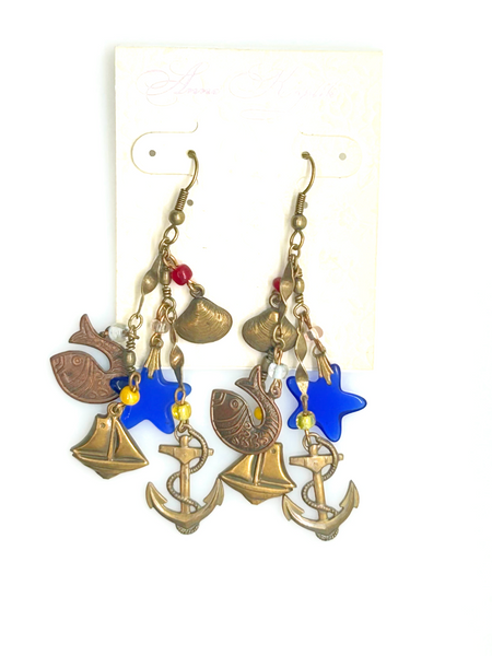 Vintage Cookie Lee nautical charm dangle earrings in antiqued brass with anchor, sailboat, fish, and blue star charms on a cream card.