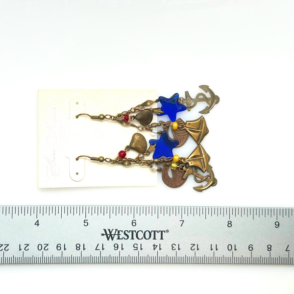 Vintage Cookie Lee nautical charm dangle earrings in antiqued brass with anchor, sailboat, fish, and blue star charms on a cream card.