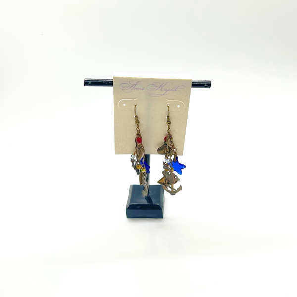 Vintage Cookie Lee nautical charm dangle earrings in antiqued brass with anchor, sailboat, fish, and blue star charms on a cream card.