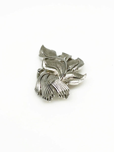An exquisite piece of vintage jewelry, the Crown Trifari Brushed Silver tone Leaf Brooch boasts eight beautifully crafted leaves, with five showcasing brushed silver tone metal and three displaying a stylized abstract design