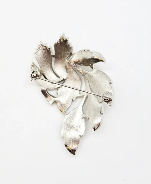 An exquisite piece of vintage jewelry, the Crown Trifari Brushed Silver tone Leaf Brooch boasts eight beautifully crafted leaves, with five showcasing brushed silver tone metal and three displaying a stylized abstract design