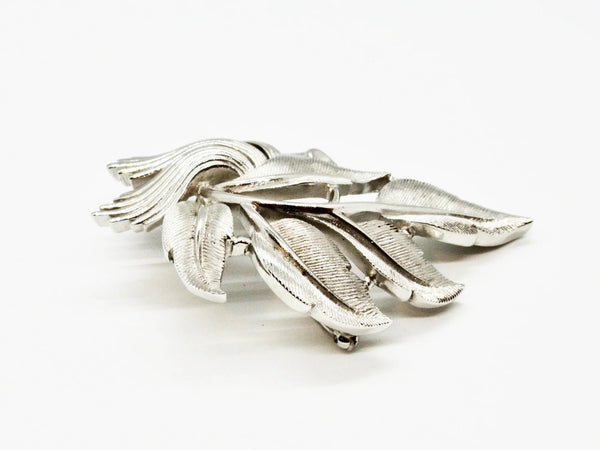 An exquisite piece of vintage jewelry, the Crown Trifari Brushed Silver tone Leaf Brooch boasts eight beautifully crafted leaves, with five showcasing brushed silver tone metal and three displaying a stylized abstract design