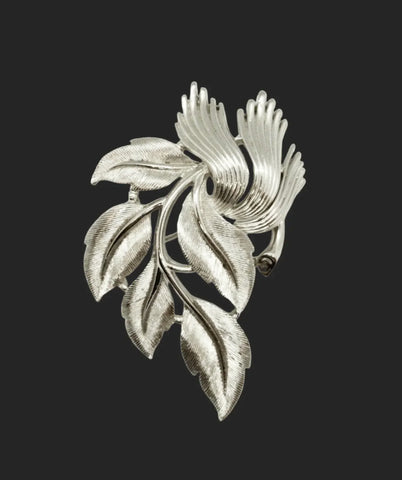 An exquisite piece of vintage jewelry, the Crown Trifari Brushed Silver tone Leaf Brooch boasts eight beautifully crafted leaves, with five showcasing brushed silver tone metal and three displaying a stylized abstract design