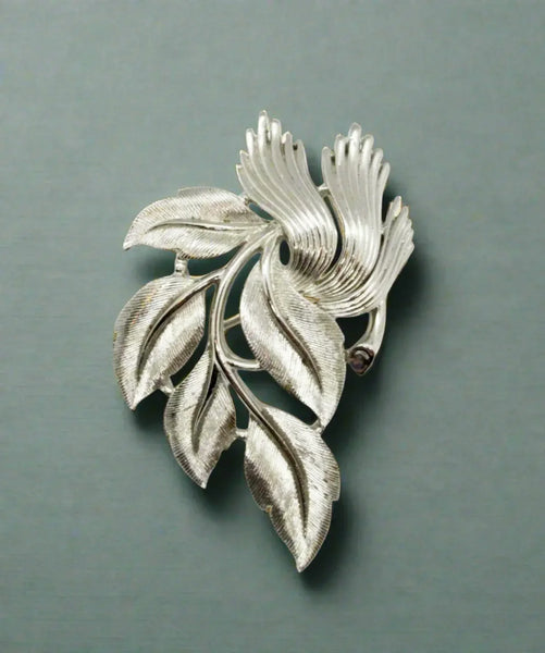 An exquisite piece of vintage jewelry, the Crown Trifari Brushed Silver tone Leaf Brooch boasts eight beautifully crafted leaves, with five showcasing brushed silver tone metal and three displaying a stylized abstract design