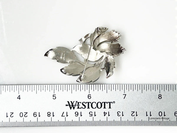 An exquisite piece of vintage jewelry, the Crown Trifari Brushed Silver tone Leaf Brooch boasts eight beautifully crafted leaves, with five showcasing brushed silver tone metal and three displaying a stylized abstract design