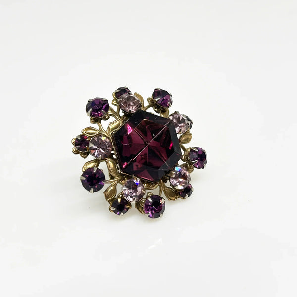 This dazzling brooch features a large octagonal purple stone at its center, surrounded by sparkling lavender and purple round stones. Its two-tiered design highlights the bezel-set centerpiece, making it truly eye-catching. With intricate details that showcase exceptional Czech craftsmanship,