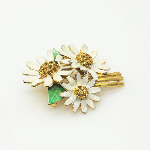 This is a cheerful vintage daisy brooch with enameled petals and a domed golden rhinestone center. It measures 2" long and is in good condition.