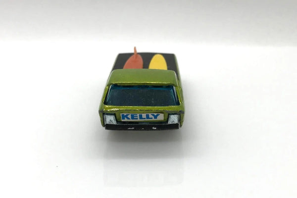 A vintage green die-cast toy car with 'KELLY' on the front, featuring a black roof with red and yellow surfboards, photographed on a white background.