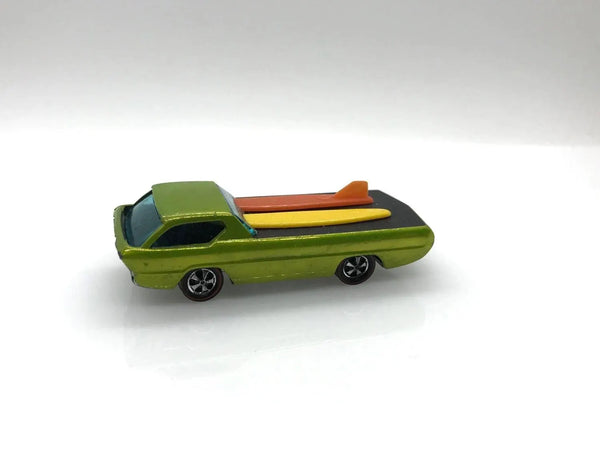 A small green toy muscle car with a black bed carrying two surfboards, one orange and one yellow, on a plain light gray background.