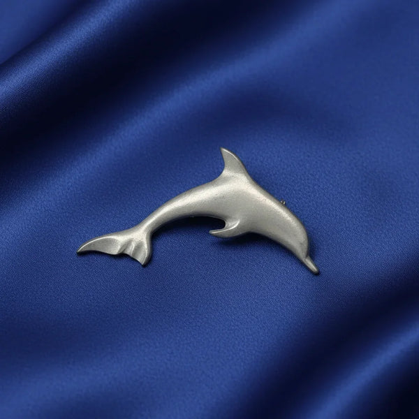 A polished silver dolphin-shaped brooch resting on a draped royal blue satin fabric background.