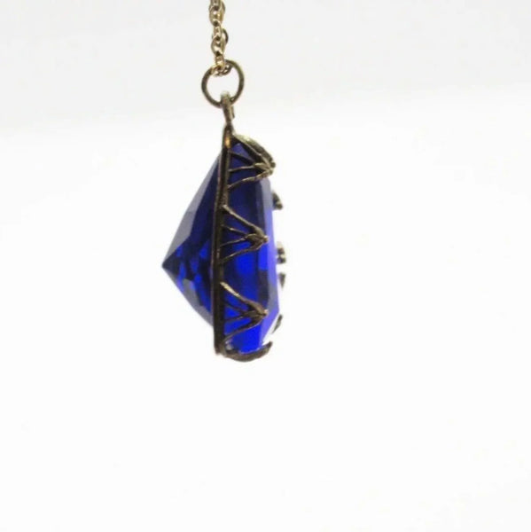 This extraordinary Art Deco pendant necklace is a true collector's treasure, featuring a stunning triangular faceted cobalt blue glass stone that shifts between rich cobalt and mesmerizing violet tones depending on the light.