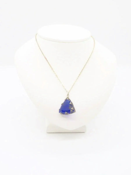 This extraordinary Art Deco pendant necklace is a true collector's treasure, featuring a stunning triangular faceted cobalt blue glass stone that shifts between rich cobalt and mesmerizing violet tones depending on the light.