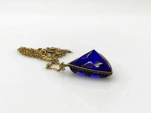 This extraordinary Art Deco pendant necklace is a true collector's treasure, featuring a stunning triangular faceted cobalt blue glass stone that shifts between rich cobalt and mesmerizing violet tones depending on the light.