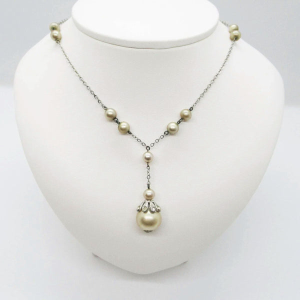 A silver-tone chain necklace with scattered pearl-like beads and a larger drop pearl pendant, displayed on a white jewelry bust against a light gray background.