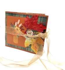 Handmade autumn mini scrapbook album featuring a green and brown plaid pattern, orange paper cover, decorative fall leaves, and a large golden ribbon bow