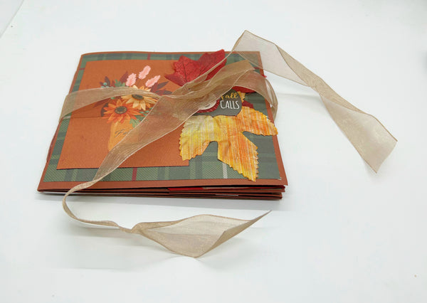 A handmade autumn-themed beige ribbon, featuring orange, red, and yellow leaf designs on a white background.