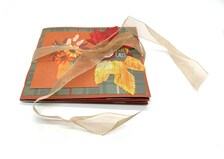 Handmade autumn mini scrapbook album featuring a green and brown plaid pattern, orange paper cover, decorative fall leaves, and a large golden ribbon bow