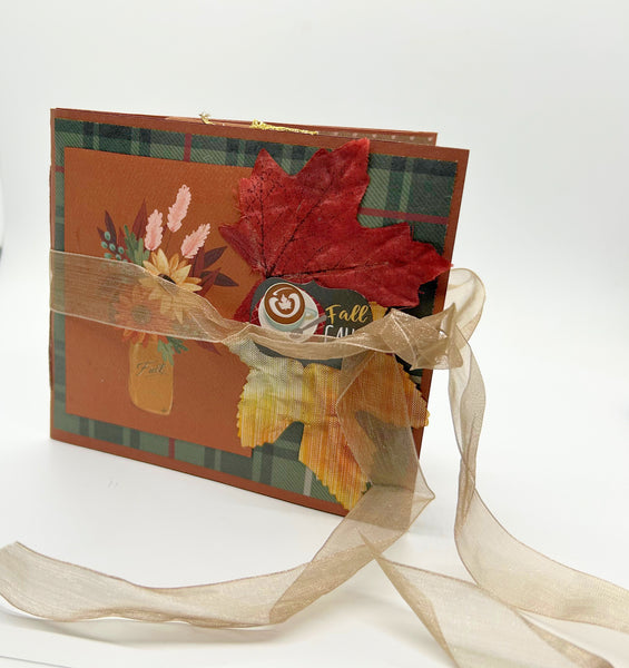 Handmade autumn mini scrapbook album featuring a green and brown plaid pattern, orange paper cover, decorative fall leaves, and a large golden ribbon bow