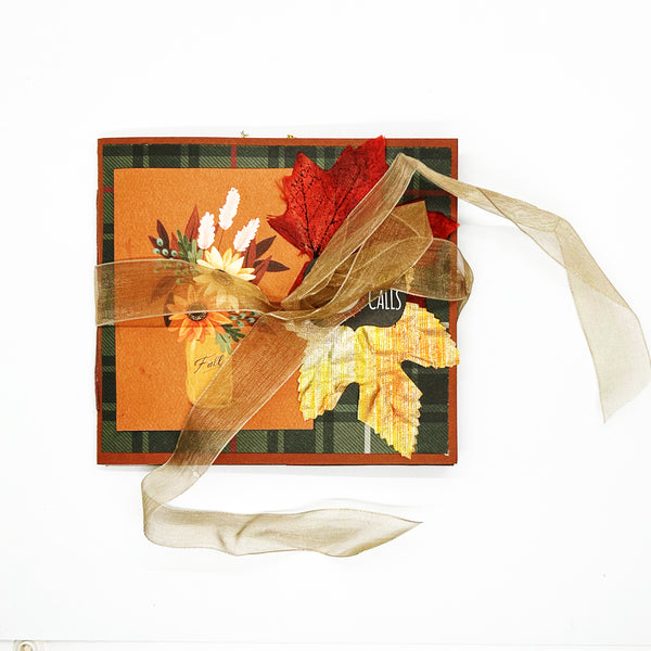 A handmade mini album with a fall theme, featuring autumnal colors, leaves, and a golden ribbon.