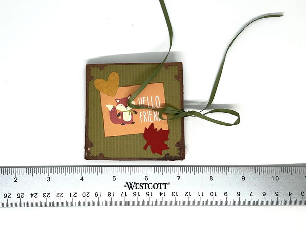 Handmade autumn mini scrapbook album featuring a green and brown plaid pattern, orange paper cover, decorative fall leaves, and a large golden ribbon bow