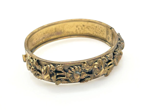 Antique goldtone floral bangle bracelet with detailed flower engravings, close-up view.