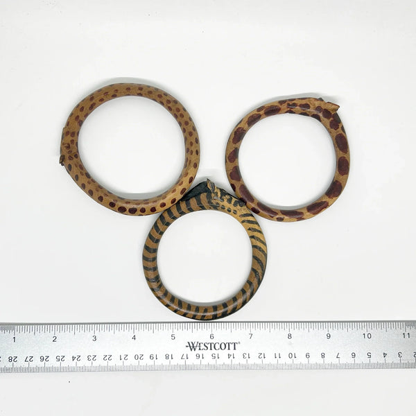 This is a set of three carved wooden bangles, with a giraffe's face carved into the side. The wood has dyed spots to emulate the animal's hide. Very Good condition. 