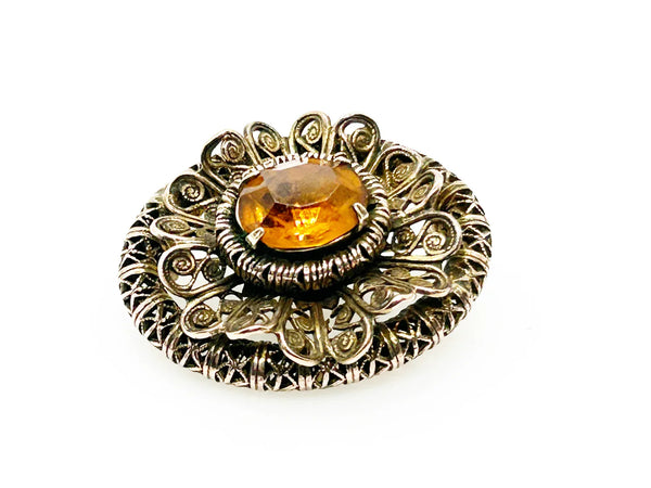 This lovely vintage brooch has a beautiful golden faceted oval stone surrounded by layers of elaborately detailed filigree. The workmanship is outstanding. The stone is prong set and secure; it's a very wearable brooch. It measures 1.5" across and is in very good condition.