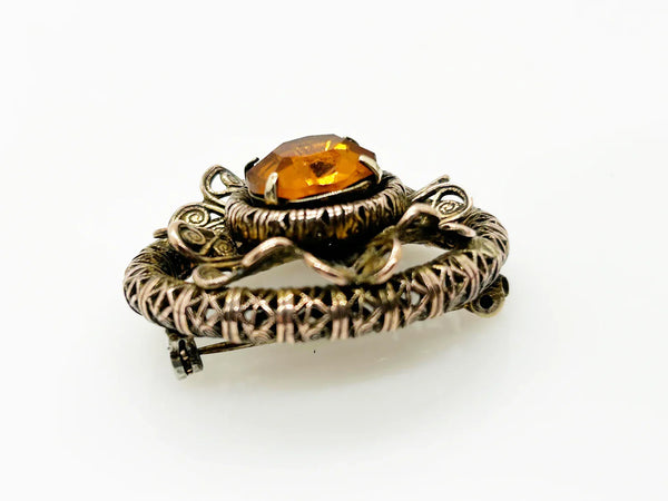 This lovely vintage brooch has a beautiful golden faceted oval stone surrounded by layers of elaborately detailed filigree. The workmanship is outstanding. The stone is prong set and secure; it's a very wearable brooch. It measures 1.5" across and is in very good condition.