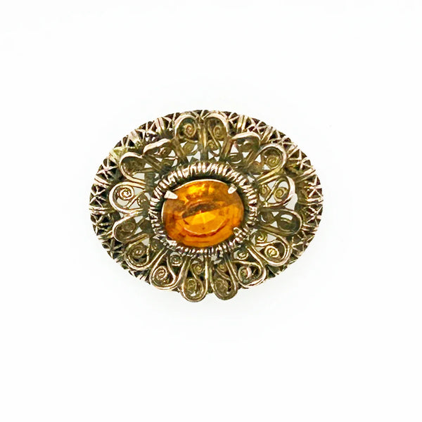 This lovely vintage brooch has a beautiful golden faceted oval stone surrounded by layers of elaborately detailed filigree. The workmanship is outstanding. The stone is prong set and secure; it's a very wearable brooch. It measures 1.5" across and is in very good condition.