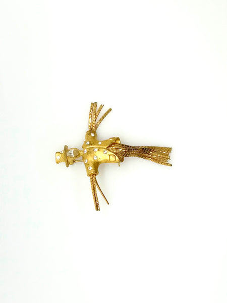 Detailed close-up of a vintage figural scarecrow brooch showing the textured metal patterns, embedded clear chaton rhinestones, and individual strands of fluid herringbone chain hanging from the tors