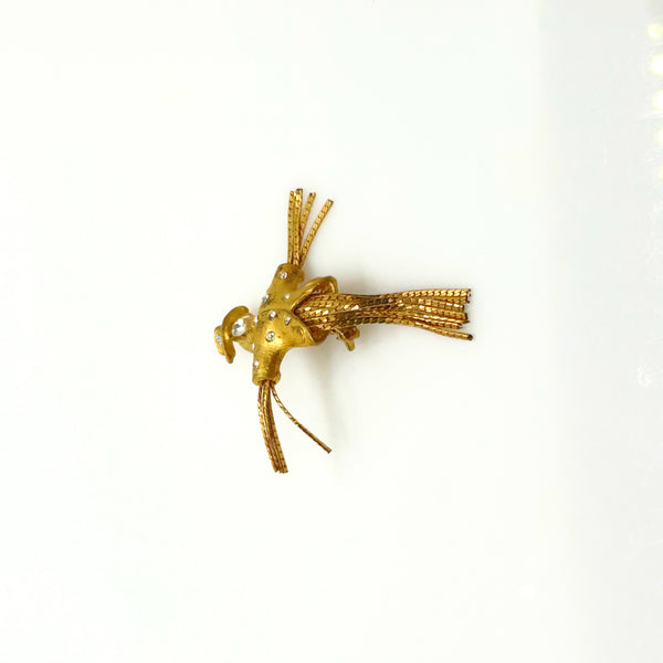 Detailed close-up of a vintage figural scarecrow brooch showing the textured metal patterns, embedded clear chaton rhinestones, and individual strands of fluid herringbone chain hanging from the tors