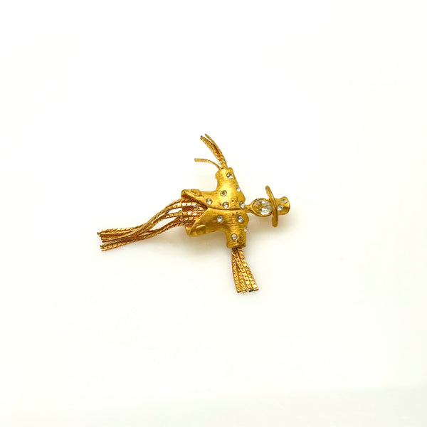 Detailed close-up of a vintage figural scarecrow brooch showing the textured metal patterns, embedded clear chaton rhinestones, and individual strands of fluid herringbone chain hanging from the tors