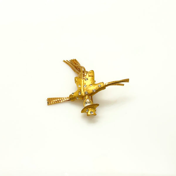 Detailed close-up of a vintage figural scarecrow brooch showing the textured metal patterns, embedded clear chaton rhinestones, and individual strands of fluid herringbone chain hanging from the tors