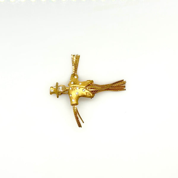 Detailed close-up of a vintage figural scarecrow brooch showing the textured metal patterns, embedded clear chaton rhinestones, and individual strands of fluid herringbone chain hanging from the tors