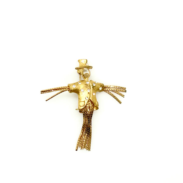 Detailed close-up of a vintage figural scarecrow brooch showing the textured metal patterns, embedded clear chaton rhinestones, and individual strands of fluid herringbone chain hanging from the tors
