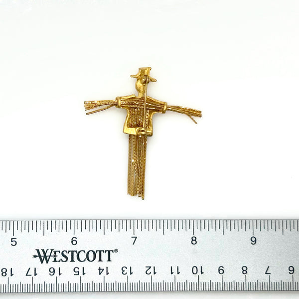 Detailed close-up of a vintage figural scarecrow brooch showing the textured metal patterns, embedded clear chaton rhinestones, and individual strands of fluid herringbone chain hanging from the tors