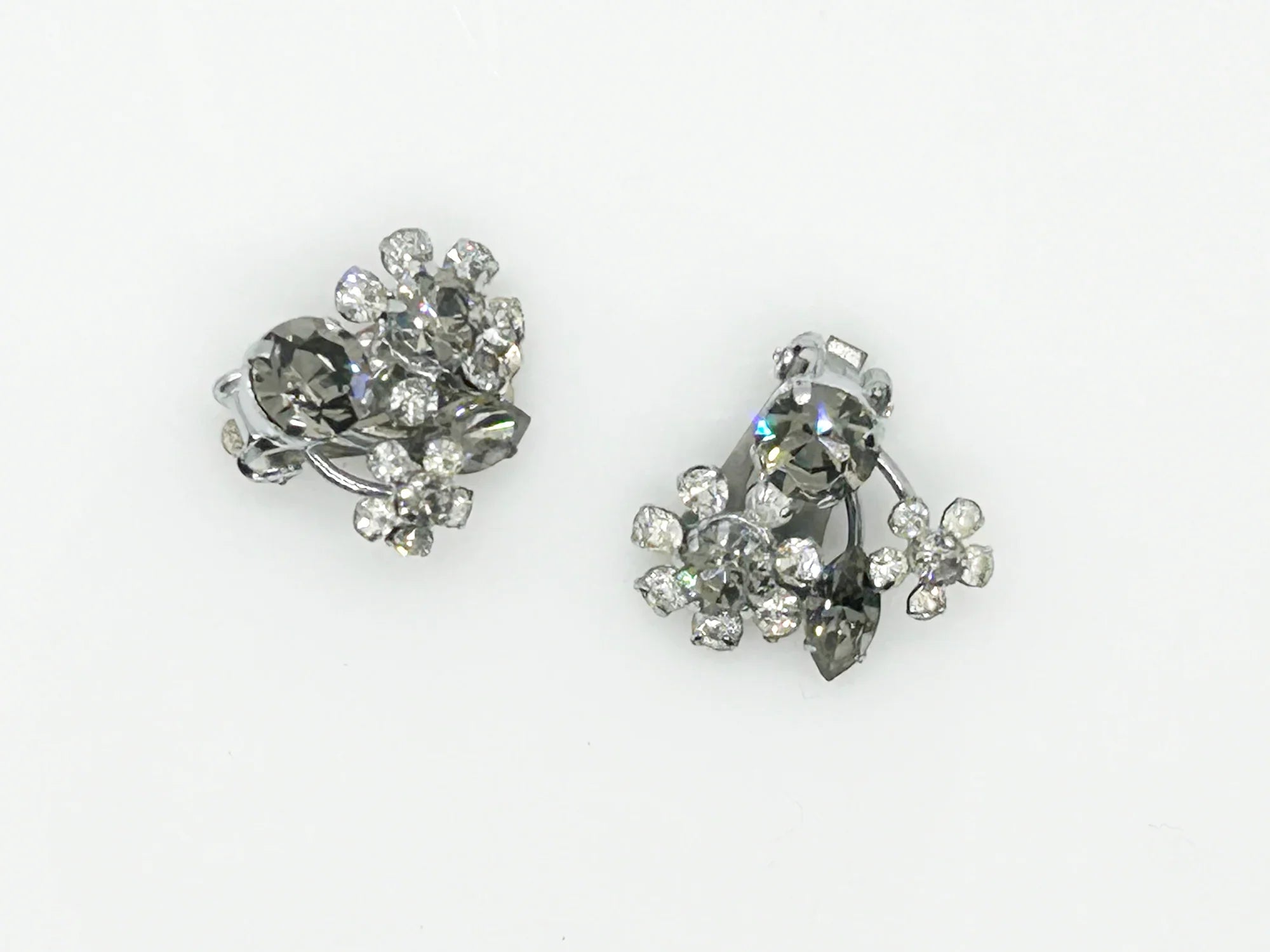 These vintage Sparkling Gray Austria Rhinestone Earrings captivate with their dazzling brilliance. Featuring a mix of gray and clear rhinestones expertly cut in marquise and round shapes, their intricate arrangement forms an elegant, eye-catching pattern