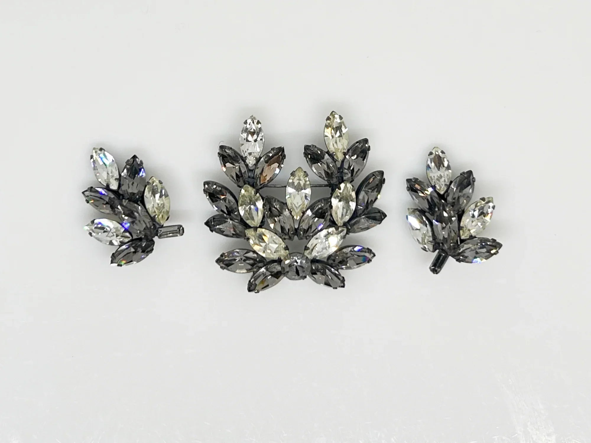 This is a gorgeous set of pin and earrings made with marquise and round shaped rhinestones in gray and clear. They are nestled in a layered, dark metal setting. The stones are standout bright and very sparking, great condition other than some wear on reverse. The earrings are clip on, hinge back.