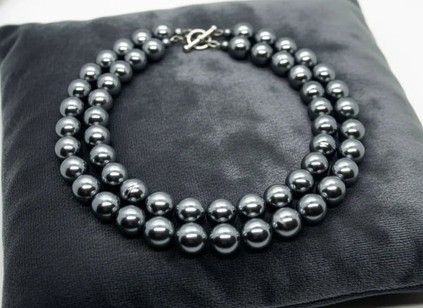 Get ready to make a statement with this stunning Vintage Double Strand of Luminous Smoky Faux Pearls Necklace! The glossy, rich gunmetal color adds a touch of elegance without being too flashy.