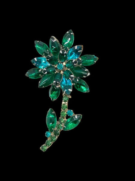 This breathtaking floral brooch embodies the essence of Juliana style with its vibrant gold tone and dazzling rhinestones. The combination of green and teal glass stones creates a mesmerizing color scheme, and its size of 3 x 1.75 x 0.625 inches is perfect for making a statement. 