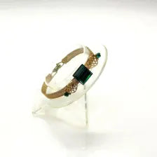 Vintage gold-tone mesh bracelet featuring a large, translucent emerald-cut green glass crystal centerpiece with delicate filigree side accents on a white display stand