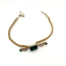 Vintage gold-tone mesh bracelet featuring a large, translucent emerald-cut green glass crystal centerpiece with delicate filigree side accents on a white display stand