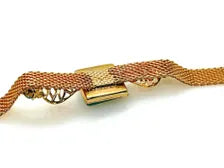 A close-up of a gold-toned chain bracelet with a decorative clasp and a textured woven or mesh-like section, shown on a plain white background.