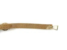 A close-up shot of a vintage gold-toned mesh bracelet, featuring a flexible, textured metal band woven into a mesh pattern.