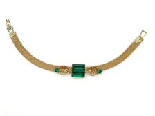 Vintage gold-tone mesh bracelet featuring a large, translucent emerald-cut green glass crystal centerpiece with delicate filigree side accents on a white display stand