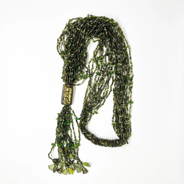 This is a substantial, but easy to wear long 1920s-30s Green Multi Strand Glass Beads Necklace. It made of of thousands of tiny beads in shades of light to deep green. Each bead catches the light and is beautiful. It is anchored by a rectangular green and gold&nbsp; bead which shimmers, introducing a timeless classic in jewelry design.