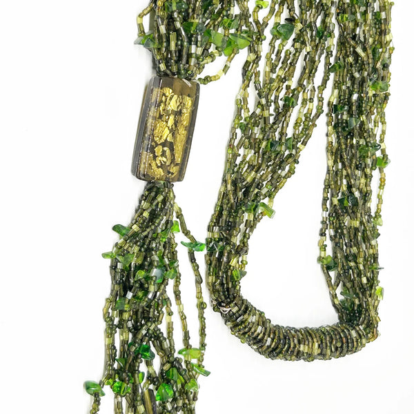 This is a substantial, but easy to wear long 1920s-30s Green Multi Strand Glass Beads Necklace. It made of of thousands of tiny beads in shades of light to deep green. Each bead catches the light and is beautiful. It is anchored by a rectangular green and gold&nbsp; bead which shimmers, introducing a timeless classic in jewelry design.